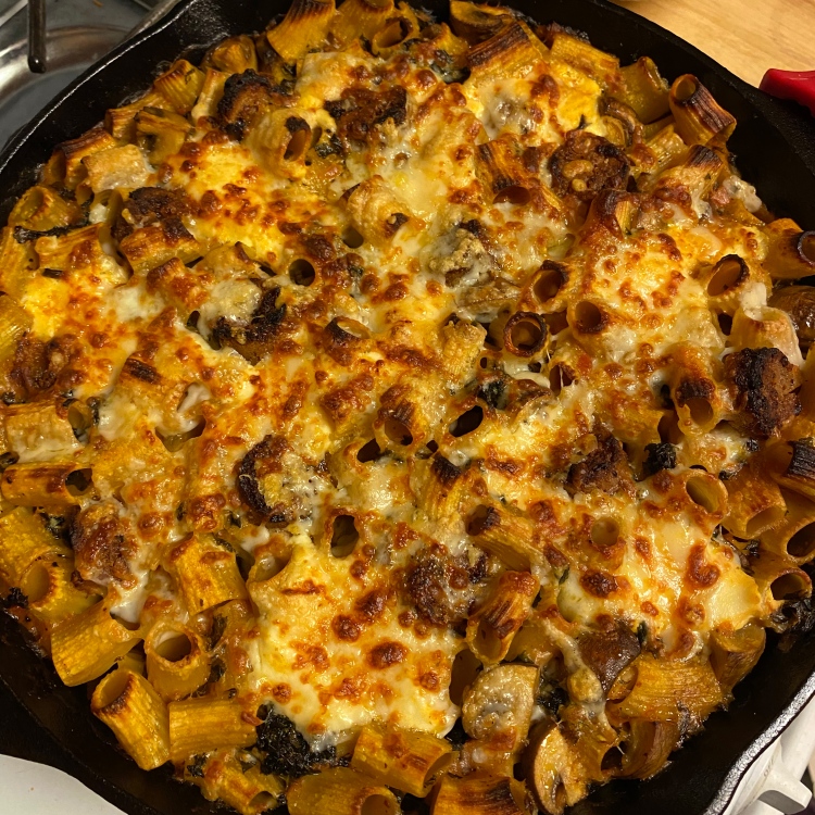 baked rigatoni pasta covered in bubbly baked cheese, in a cast iron pan