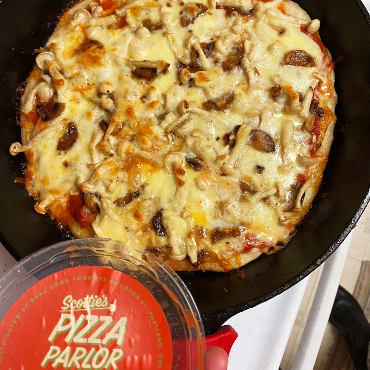 an uncut pizza in a black cast iron pan with the toppings listed in the caption plus lots of cheese, and part of the lid of the Scottie's sauce container