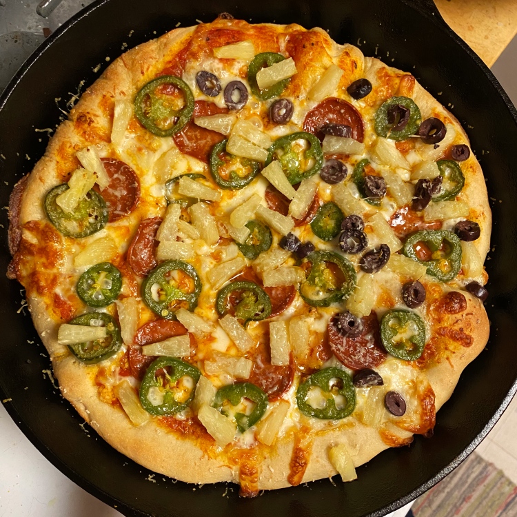 an uncut pizza in a black cast iron pan with the toppings listed in the caption plus lots of cheese