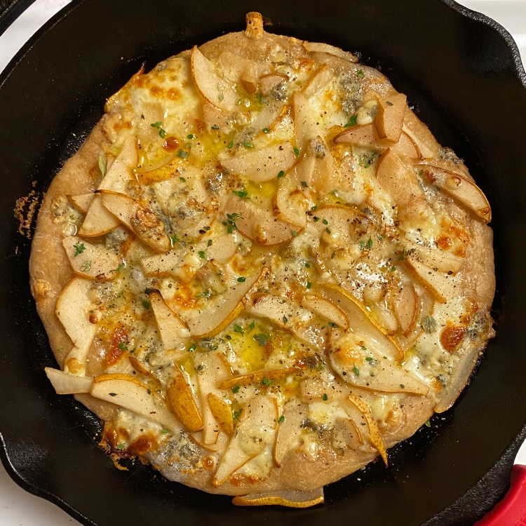 an uncut pizza in a black cast iron pan with the toppings listed in the caption