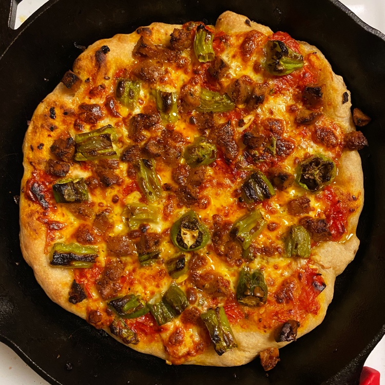 an uncut pizza in a black cast iron pan with the toppings listed in the caption plus lots of cheese