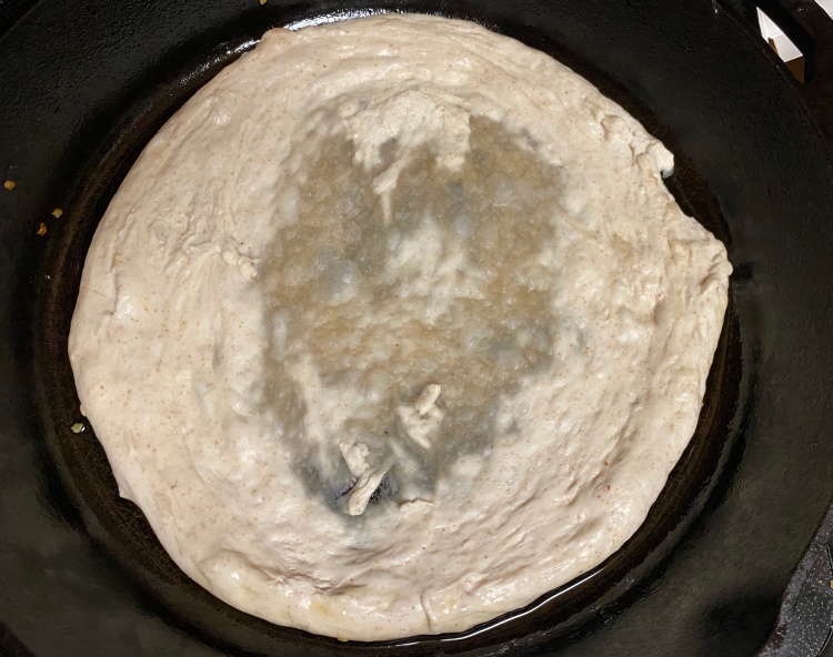 pizza dough stretched in cast iron pan, with some rips patched up by torn off pieces of dough