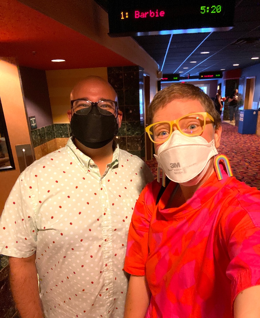 Lee and Pete wearing colorful clothes and masks in front of a movie sign that says Barbie 5:20