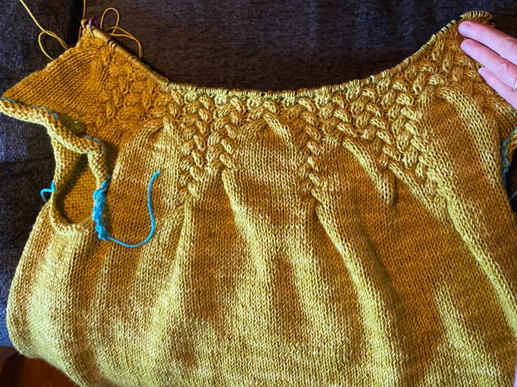 in-progress sweater with several inches of the yoke worked, crochet-chain provisional stitches where the sleeves will go