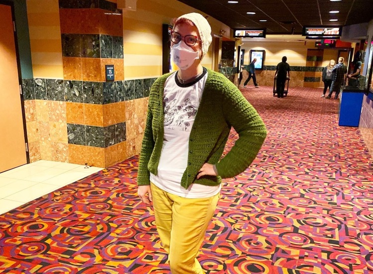 Lee wearing a mask and a green cardigan in a movie theater