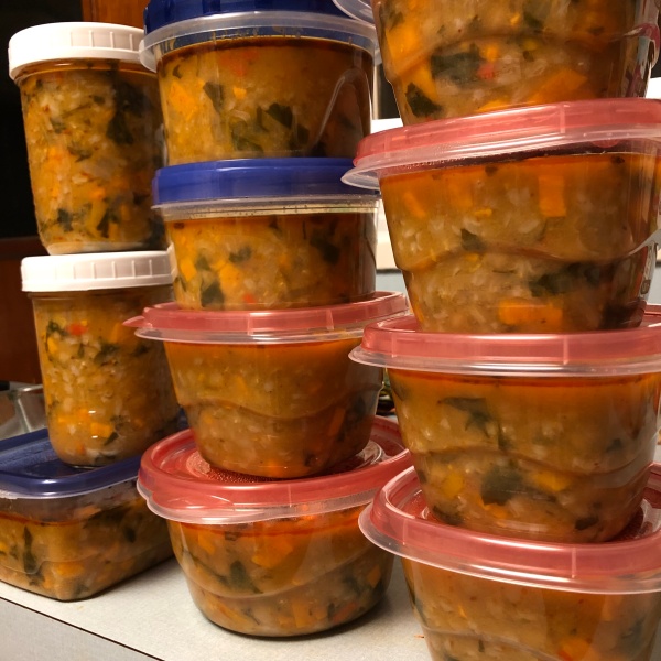 11 containers full of orange-ish soup with chunks of sweet potato and kale showing